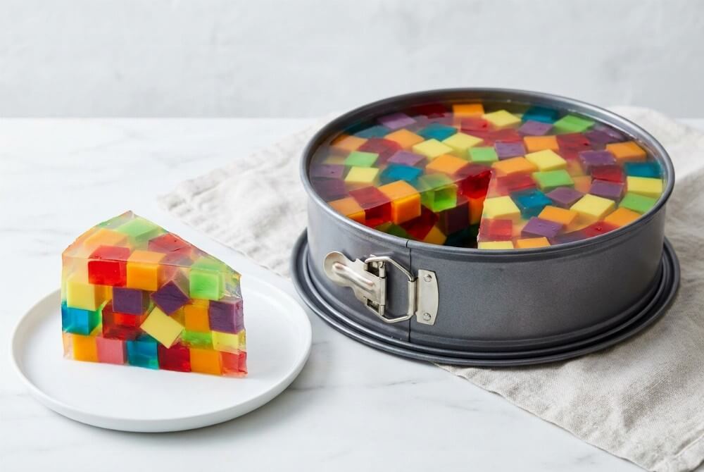 Galaretkowy tort z kolorowych kostek, na talerzyku plaster z wyraźną mozaiką barwnych sześcianów.