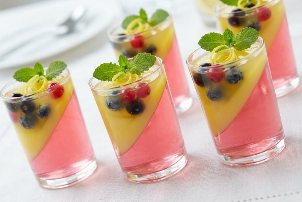 Dwukolorowe mini deserki w kieliszkach z owocami w galaretce i dekoracją z mięty.