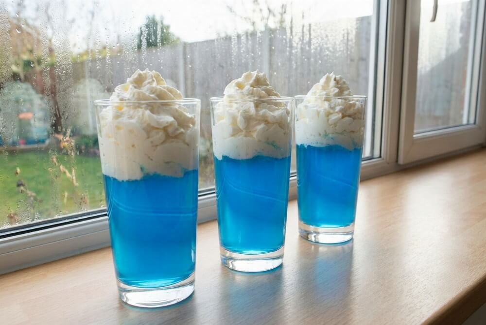 Szklanki z niebieską galaretką i białymi „chmurkami” z bitej śmietany na jasnym blacie