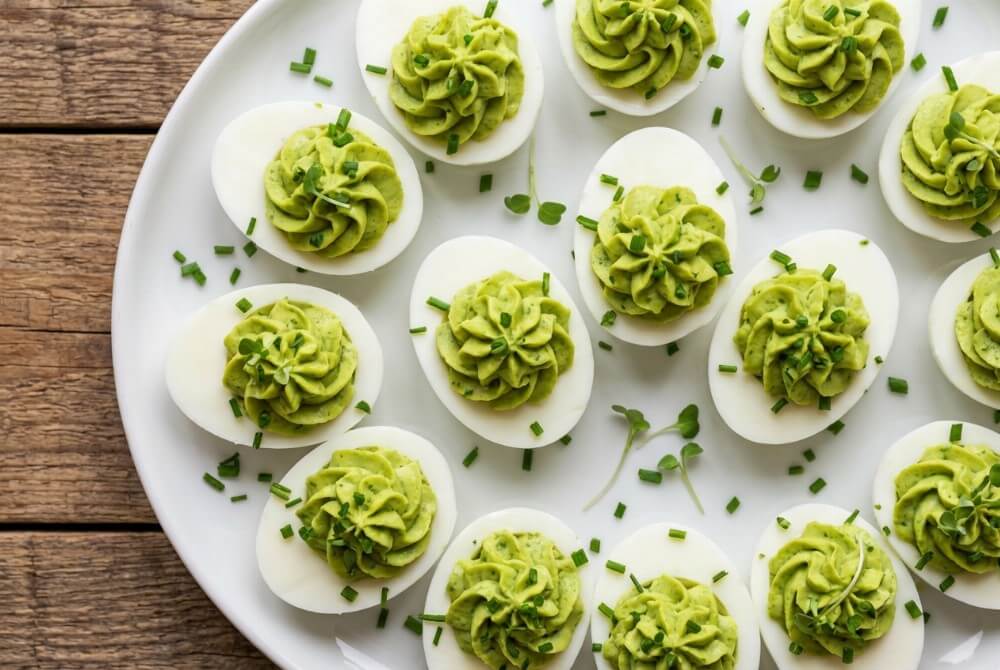 Jajka faszerowane kremową pastą z awokado i szczypiorkiem na talerzu.
