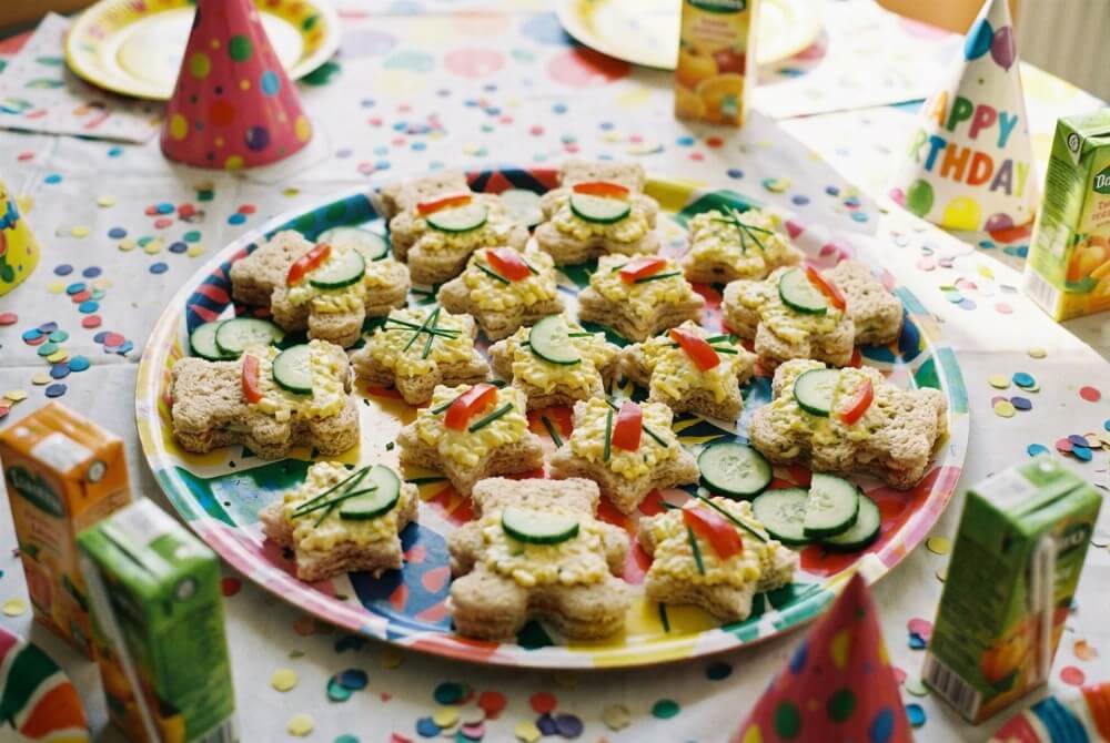 Mini kanapeczki w kształcie zwierzaków z pastą jajeczną i warzywami na tacy urodzinowej.