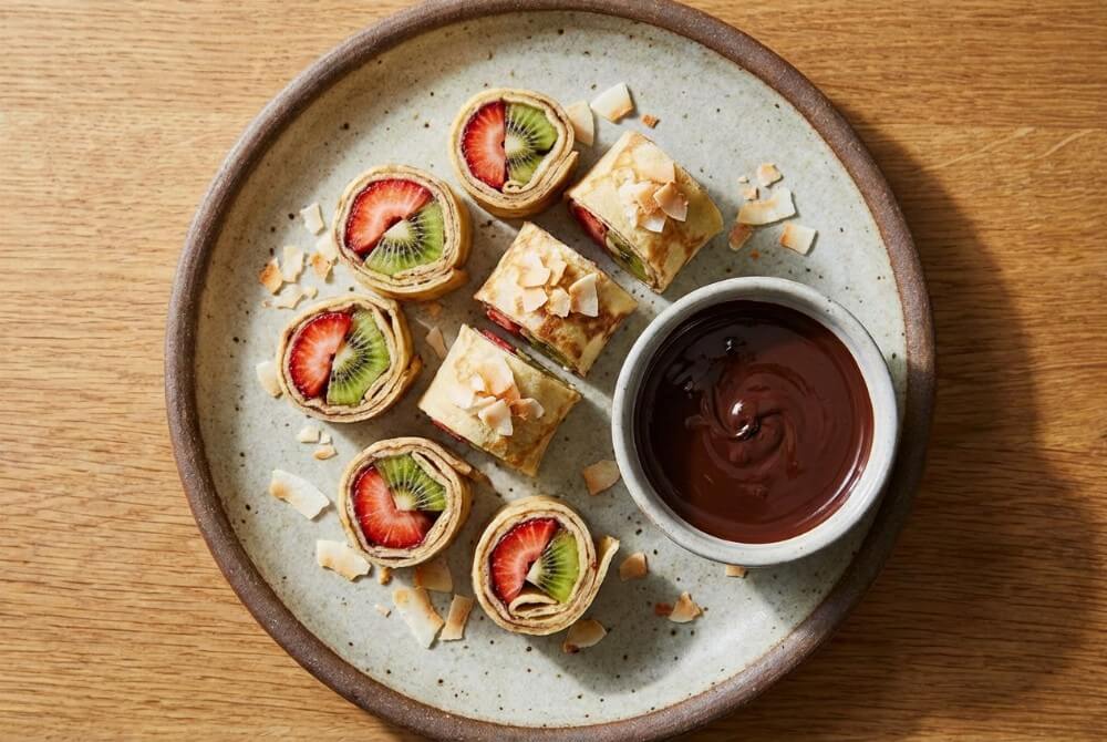 Owocowe sushi z naleśników z truskawkami i kiwi, podane z czekoladą.