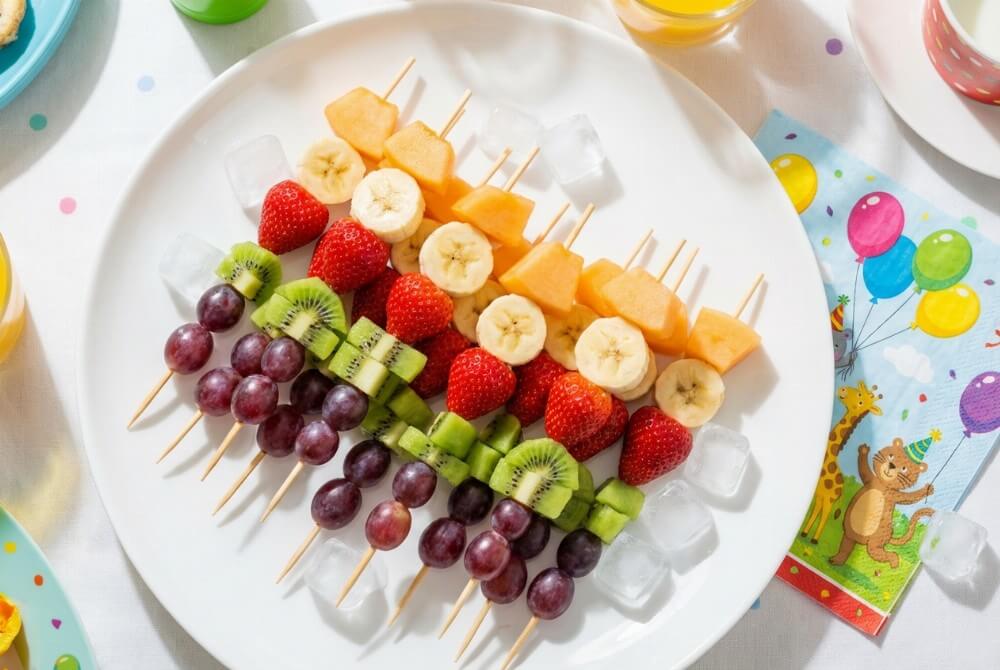 Tęczowe szaszłyki z kolorowych owoców na półmisku na przyjęciu dla dzieci.