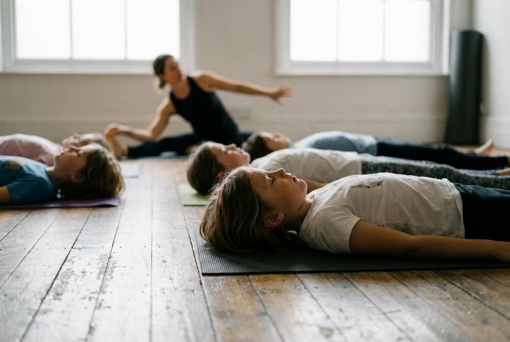 Dzieci na warsztatach ruchowych wykonują proste pozycje jogi i ćwiczenia relaksacyjne na matach.