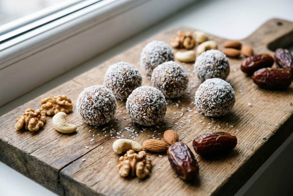 Kulki mocy z daktyli i orzechów obtoczone w wiórkach kokosowych na desce, obok daktyle i orzechy.