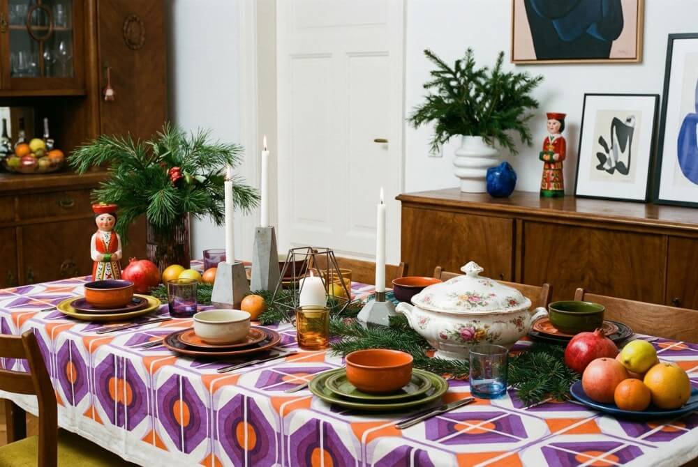 Kolorowy i eklektyczny stół wigilijny w stylu retro z geometrycznymi dodatkami i kontrastową ceramiką.