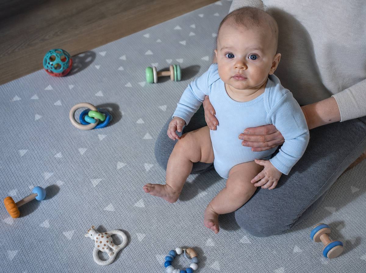 Czteromiesięczne niemowlę trzymane w siadzie z podparciem, dłonie opiekuna na klatce piersiowej