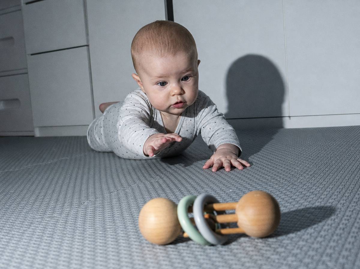 Niemowlę podczas tummy time unosi głowę, sięgając po zabawkę leżącą poza zasięgiem