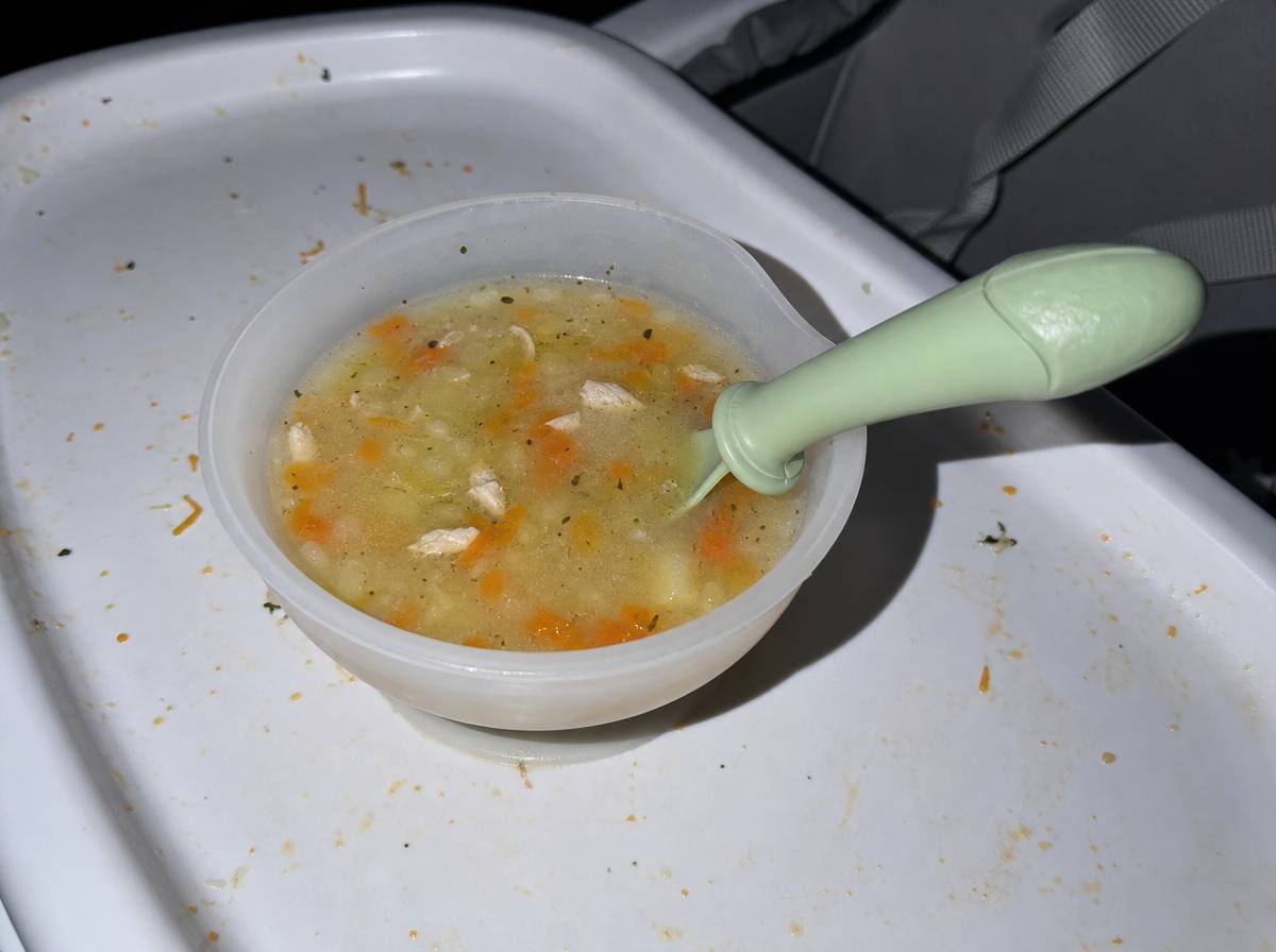 Zupa jarzynowa z kawałkami indyka i warzyw podana niemowlakowi w miseczce